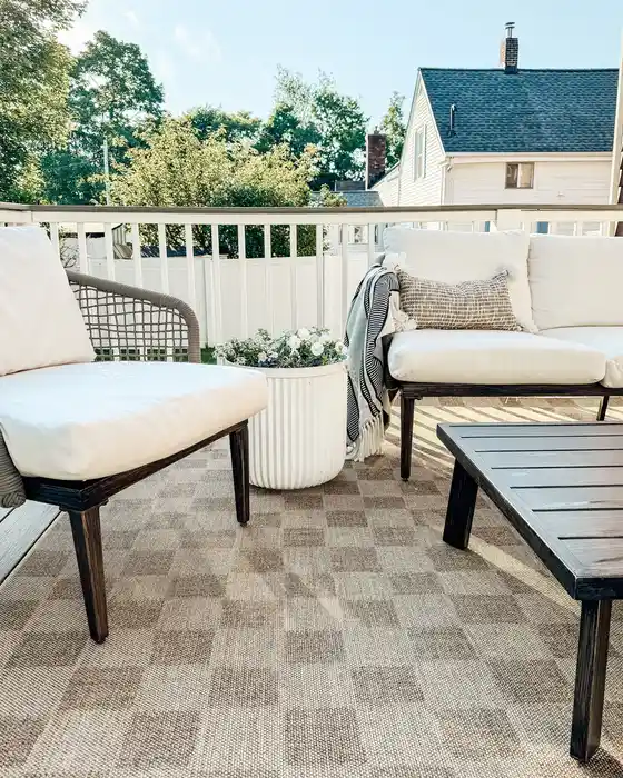Light checkerboard outdoor rug on a small balcony with pale seating and a dark table frame.