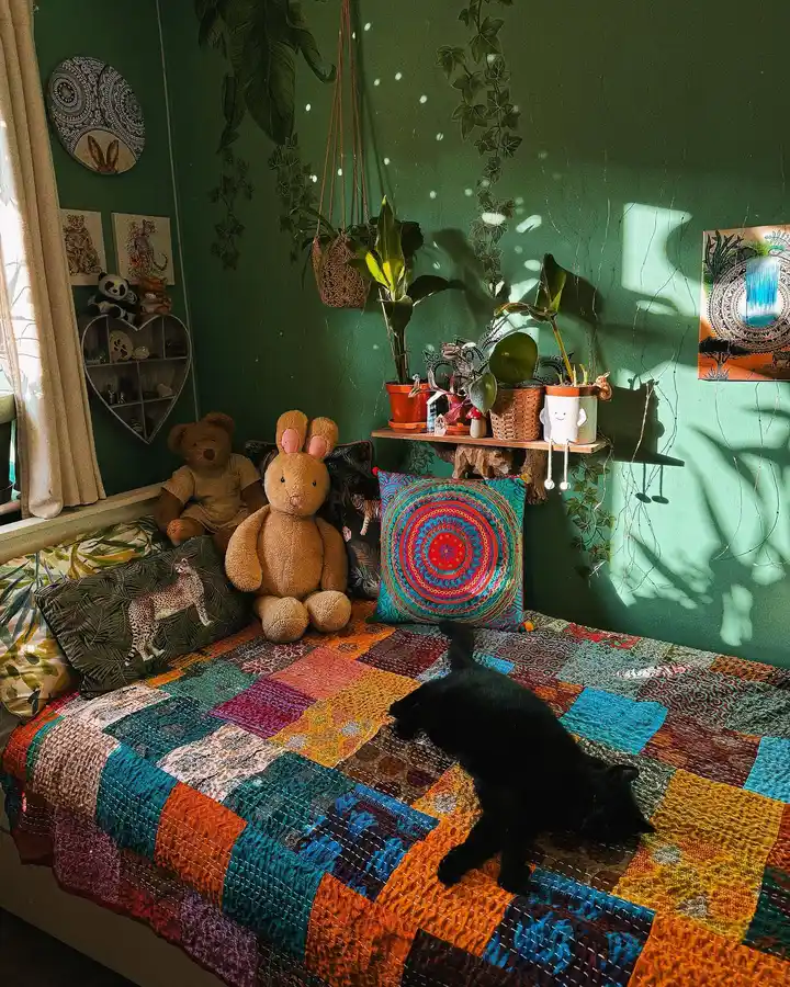 Boho bedroom with deep green walls, colorful patchwork quilt, layered pillows, hanging plants, woven baskets, and natural wood decor