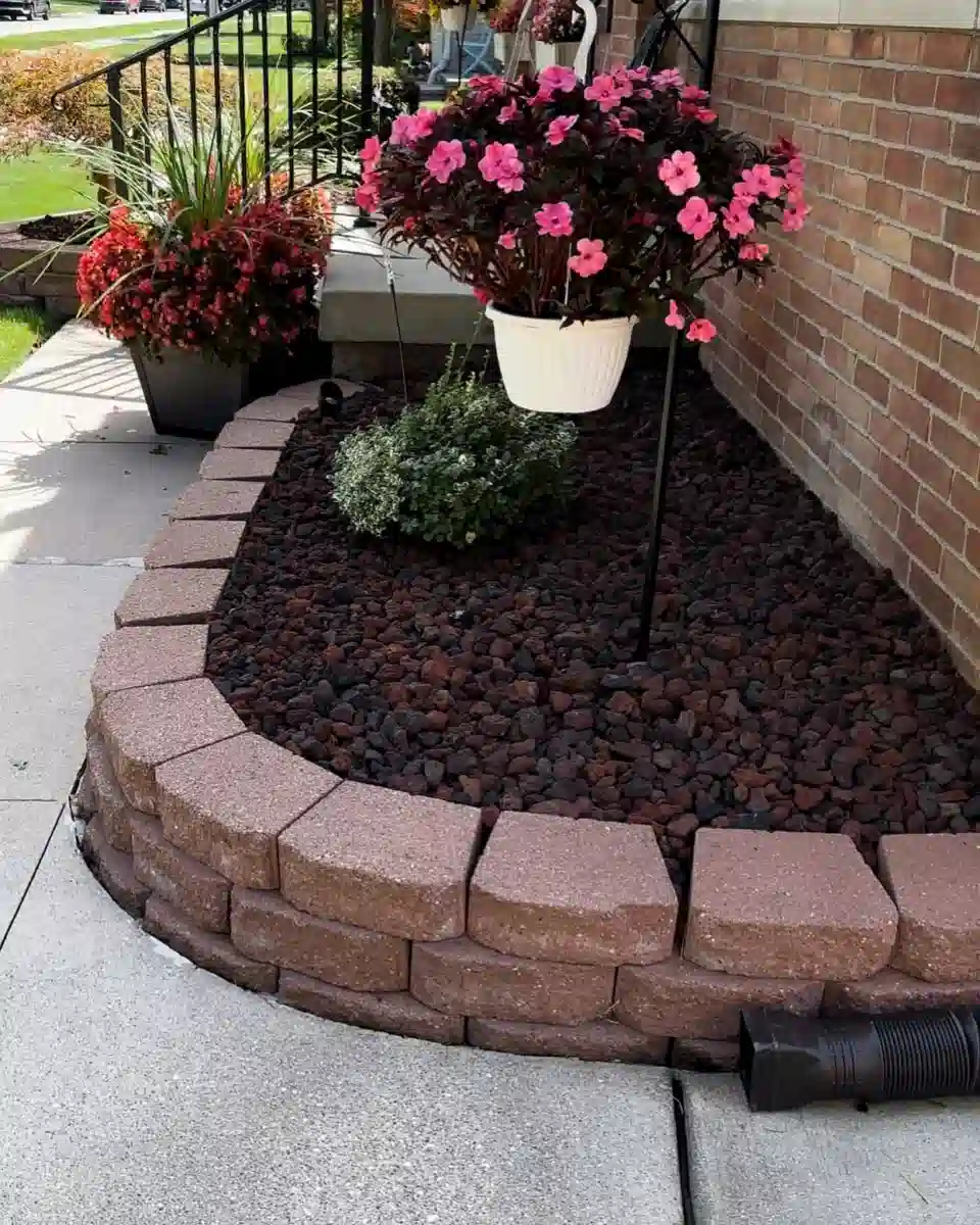 Pink flowers in a raised garden bed edged with reddish-brown bricks beside pale paving.