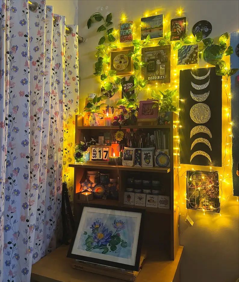Dark dorm desk setup with moon wall art, plants, warm string lights, and cozy lighting