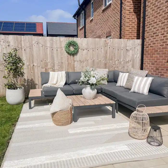 Gray and white striped outdoor rug beneath a sofa and coffee table on a narrow brick patio.
