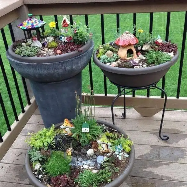Three separate fairy garden pots filled with miniature houses, plants, stones, and fairy decorations