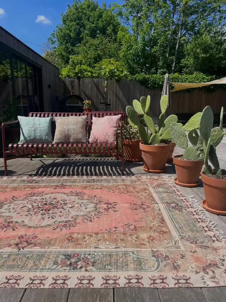 Faded vintage floral outdoor rug with muted red and sandy tones in a garden seating area.