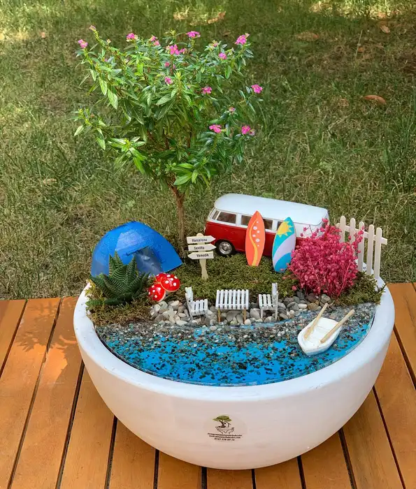Miniature fairy garden with a tiny pond, bridge, flowers, stones, and small fairy figures