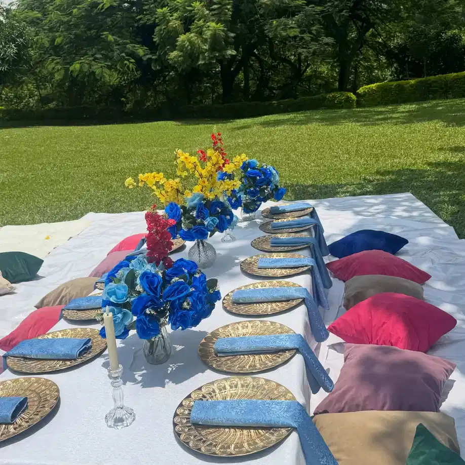 Outdoor table with blue napkins, blue flowers, white tablecloth, and woven gold-toned placemats