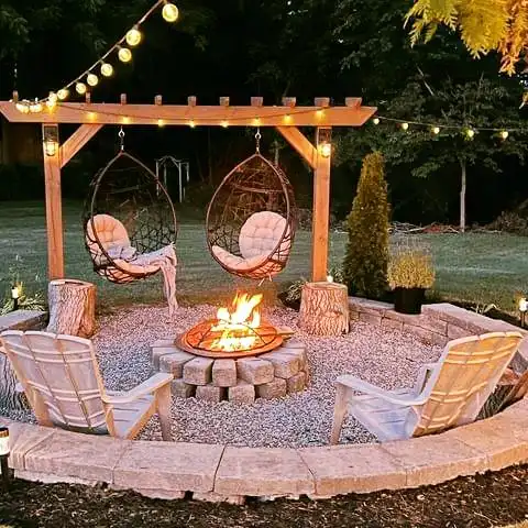 Backyard fire pit beneath a wooden pergola with hanging chairs, outdoor seating, and string lights