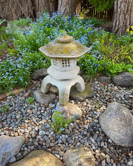 Traditional Japanese stone lantern surrounded by pebbles, moss, and small blue flowers