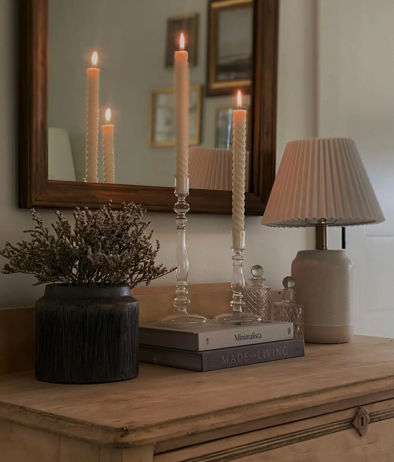 Dresser styled with clear glass candlesticks, pleated lamp, dark vase, dried stems, and stacked books