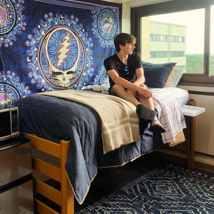 Dorm room with a large blue patterned tapestry above neutral cream, gray, and navy bedding