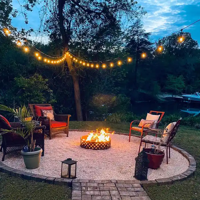 Round backyard fire pit surrounded by outdoor chairs beneath overhead string lights