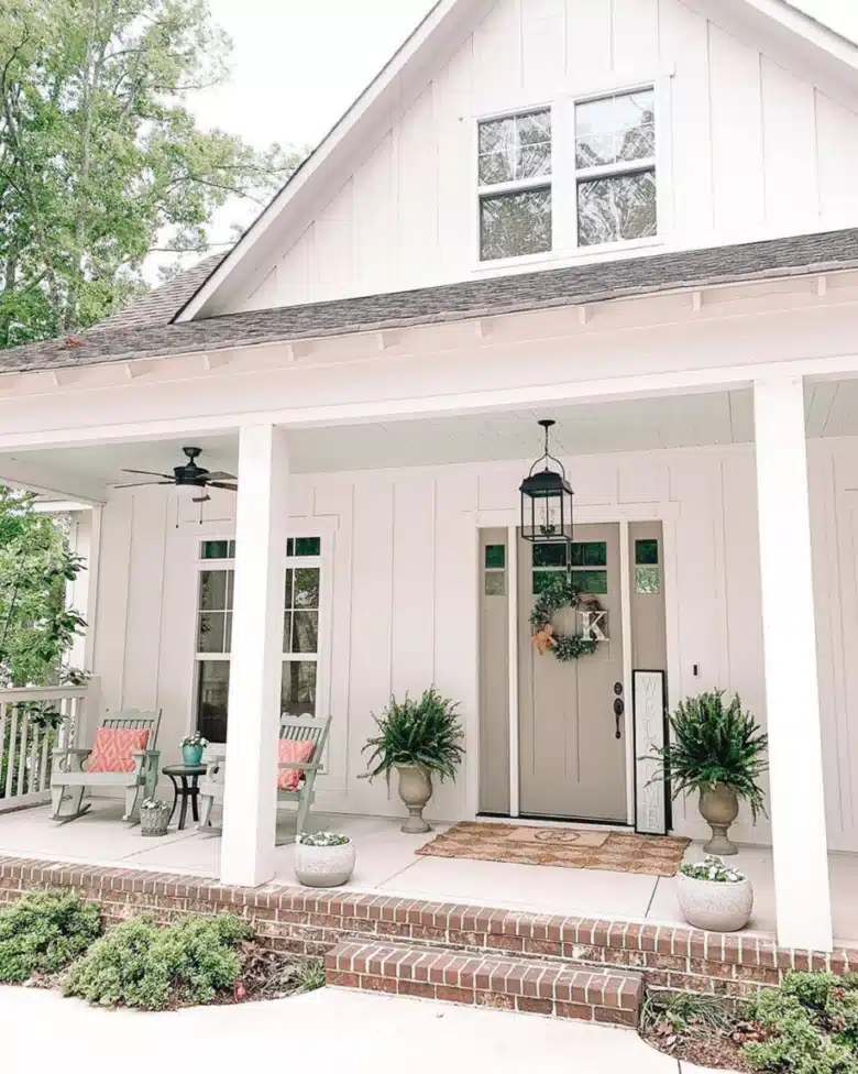 White farmhouse exterior with white rocking chairs, open front steps, and a few potted plants