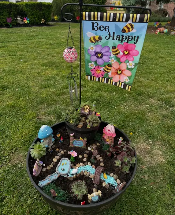Small fairy garden with a miniature garden sign surrounded by flowers, greenery, and tiny decorations