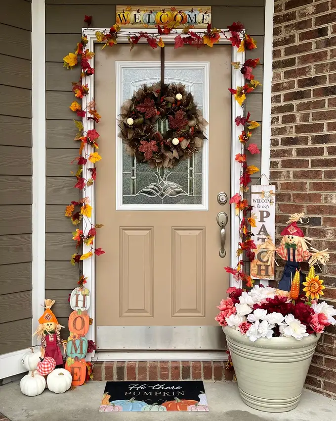 Fall front door decor with a leafy wreath, pumpkins, orange flowers, and autumn planters