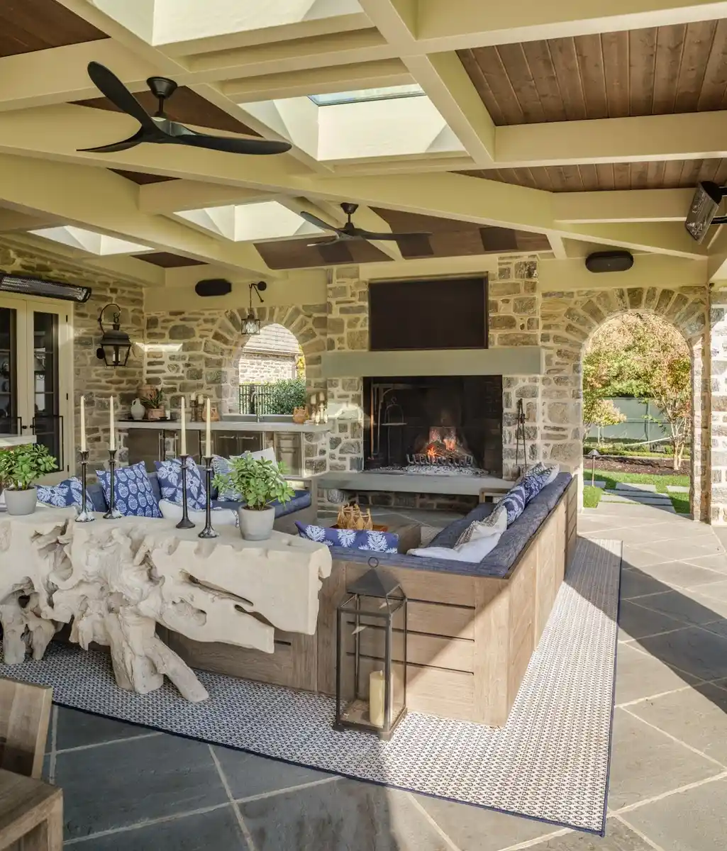 Large covered porch with seating, stone fireplace, wood ceiling, skylights, and outdoor views
