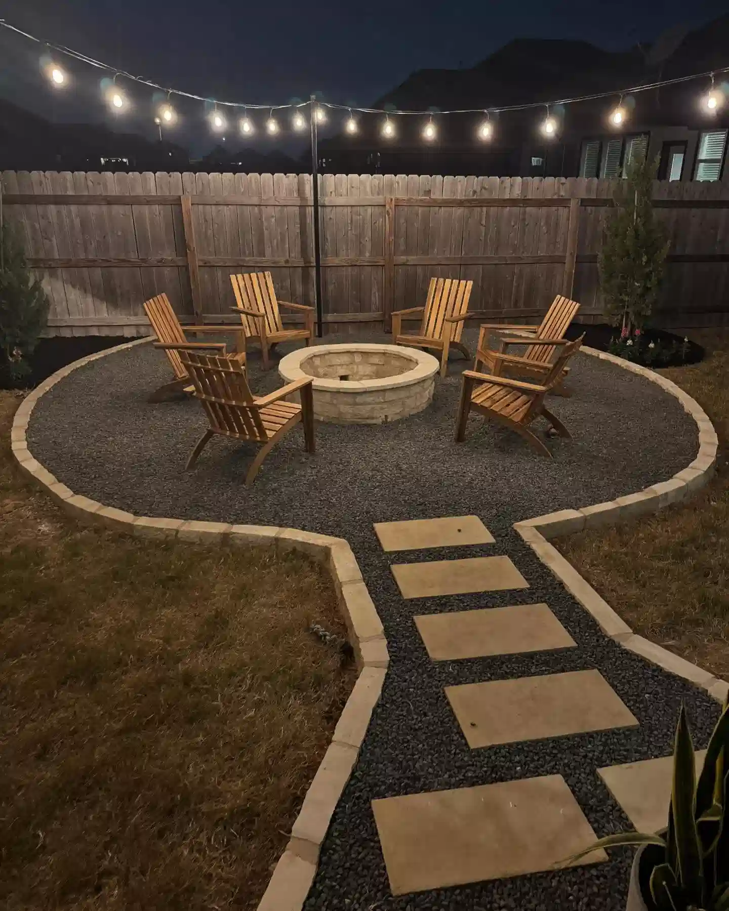 Outdoor string lights framing a curved stepping-stone garden path and seating area