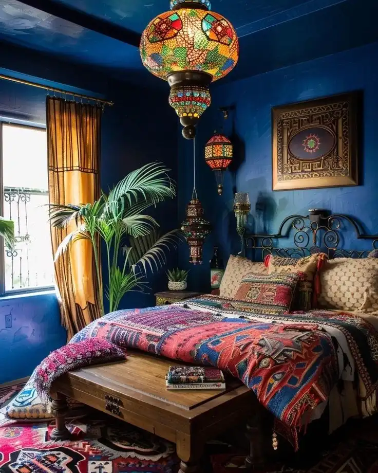 Boho bedroom with deep cobalt blue walls and ceiling, amber curtains, colorful lanterns, patterned bedding, and carved wood furniture