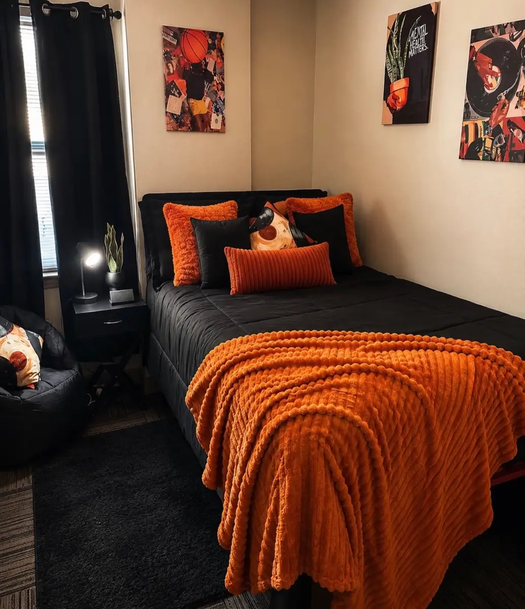 Black dorm room bedding with an orange throw, orange pillows, and warm-toned wall art