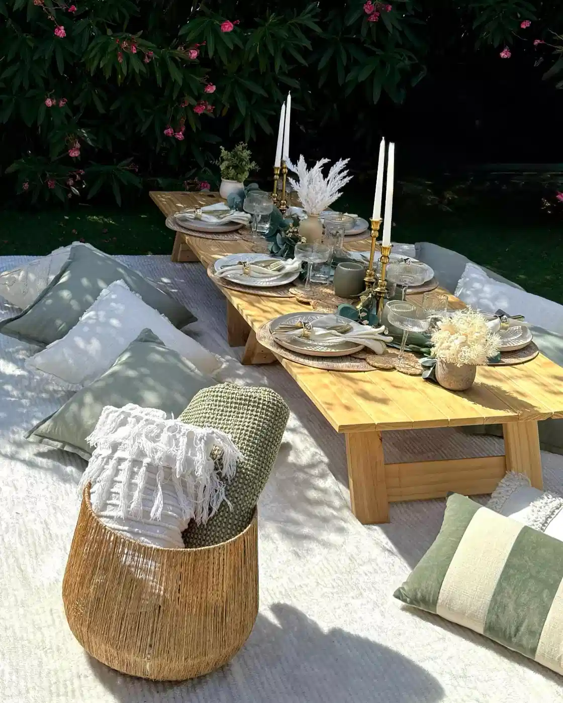 Low wooden picnic table with floor cushions and a simple floral centerpiece in an outdoor setting