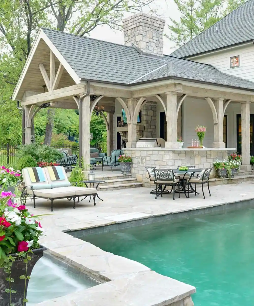 Poolside covered porch with dining table, lounge chairs, white columns, and flower planters