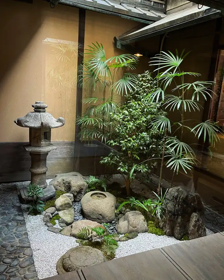 Small Japanese courtyard with a slender bamboo plant, stone water basin, pebbles, and wooden wall