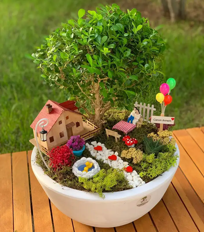 Low fairy house surrounded by moss, white flowers, stones, and miniature garden details