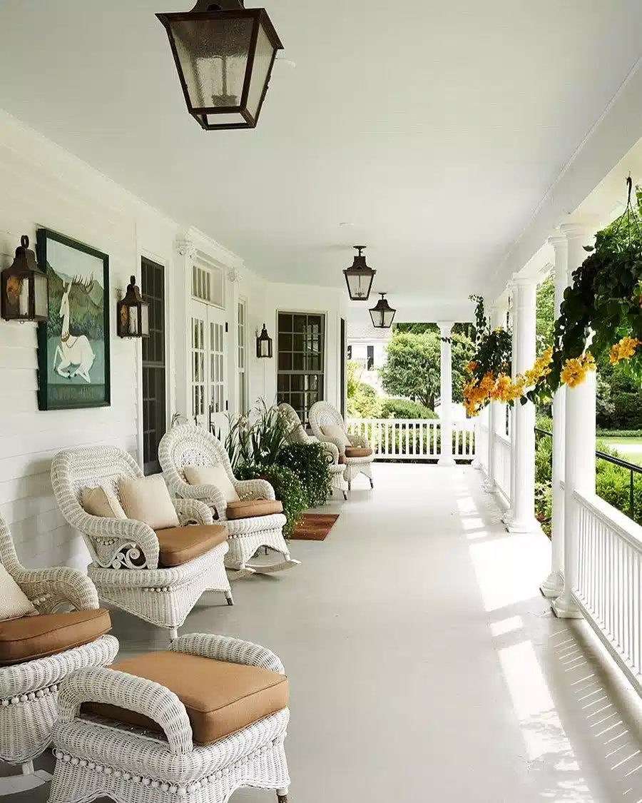 Long white farmhouse porch with multiple seating areas, pale furniture, and ceiling lights