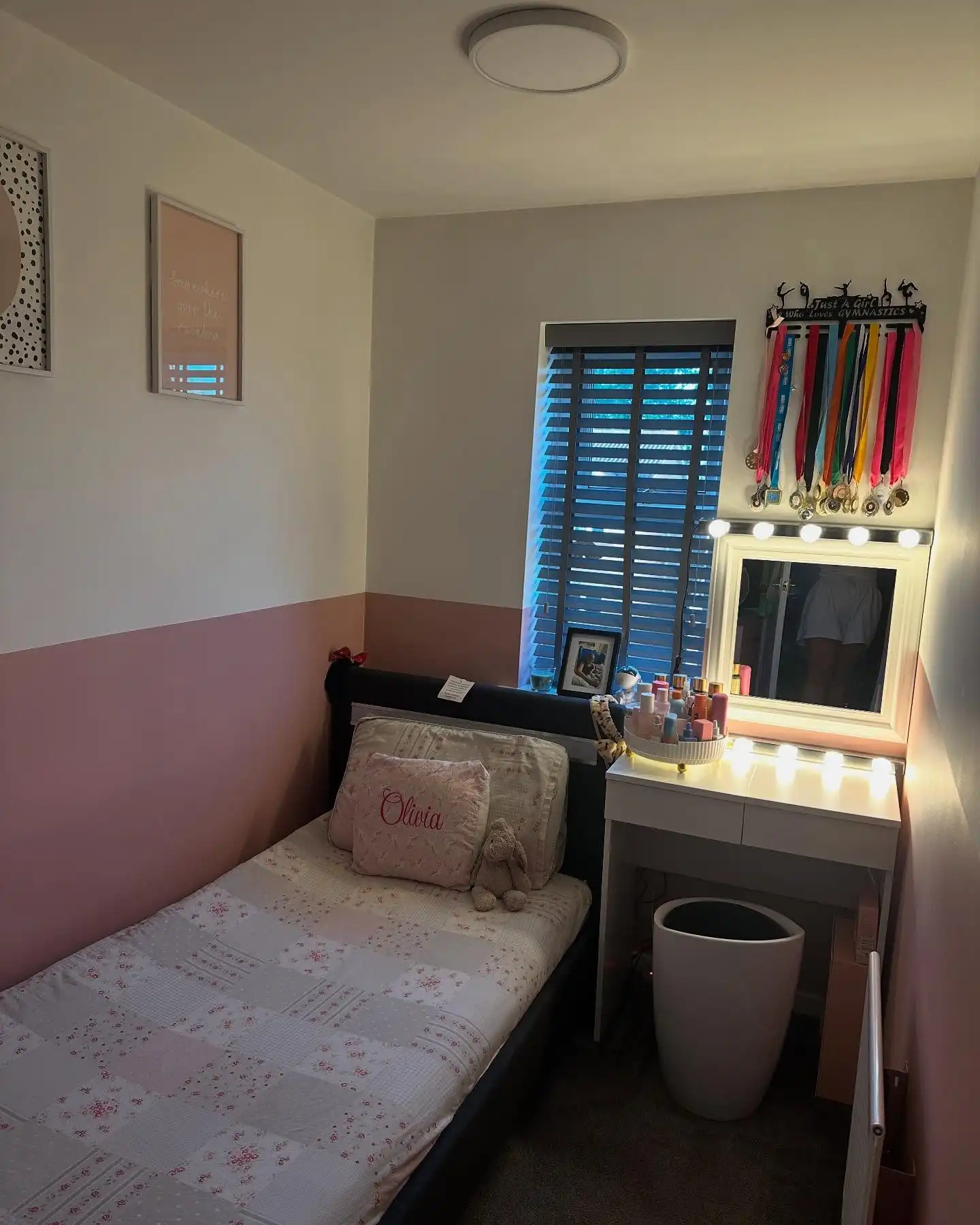 Small kids bedroom with single bed, narrow lighted vanity, stool, and wall-mounted medal display