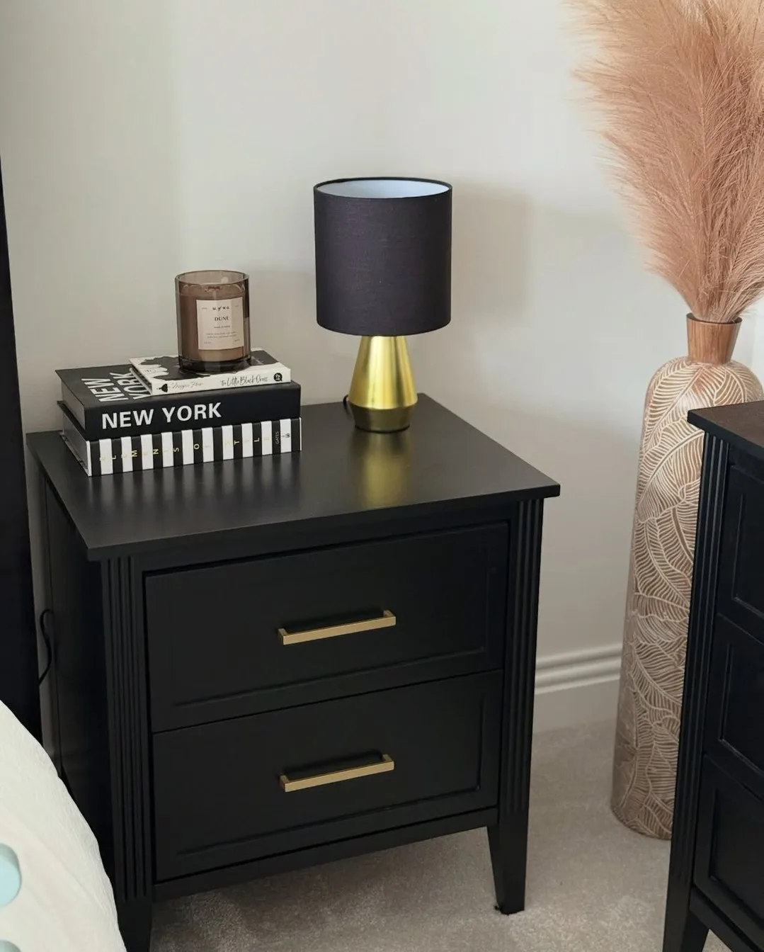 Black nightstand with black lamp shade, brass details, candle, and stacked dark books