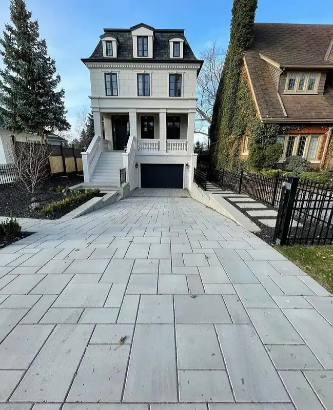 Large-format rectangular pavers covering a broad driveway leading toward a tall modern house