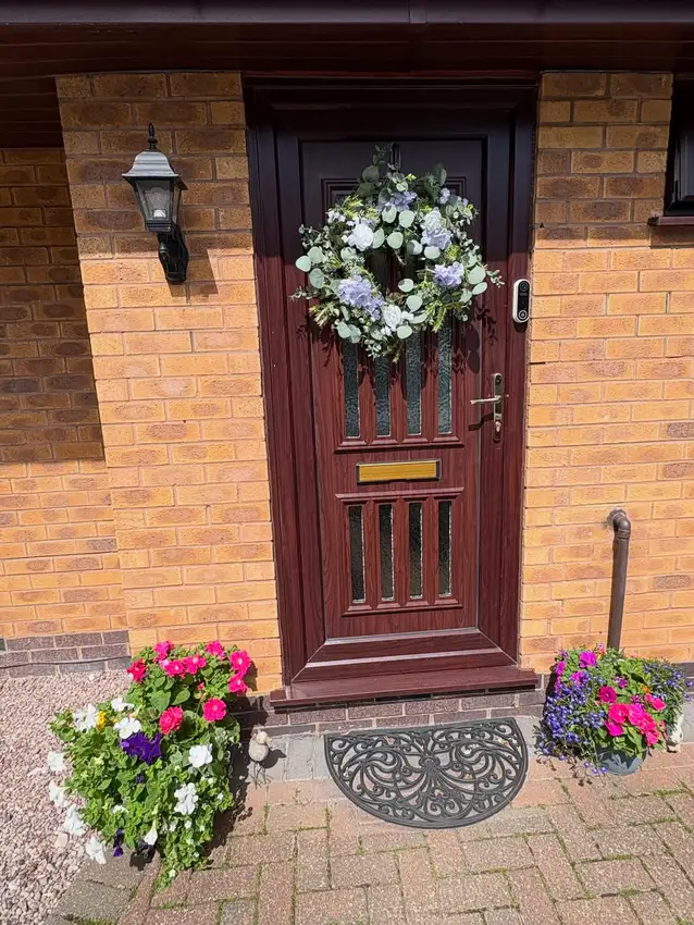 Burgundy front door with pink and white flowers in large planters beside a brick entrance