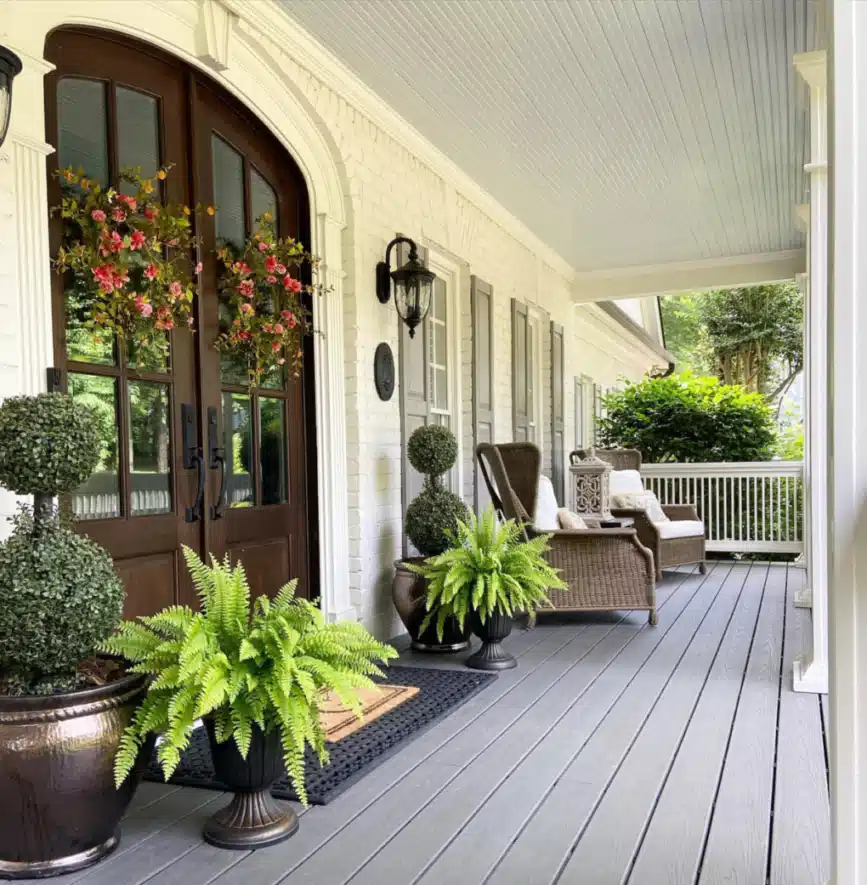 Covered farmhouse porch with dark planters, leafy green plants, and a pale ceiling
