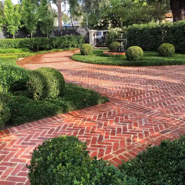 Curved brick driveway winding through rounded shrubs and neatly clipped garden greenery