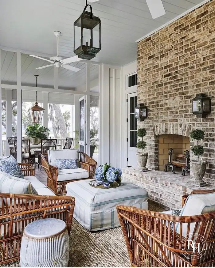 Covered porch with wicker seating, large stone fireplace, pale cushions, and outdoor rug