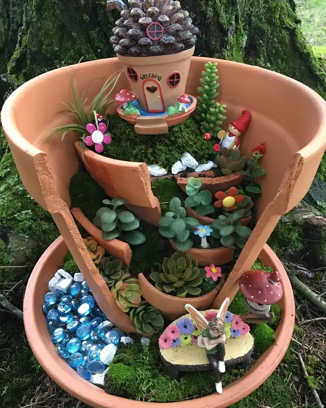 Broken terracotta pot transformed into a multi-level fairy garden with miniature figures and plants