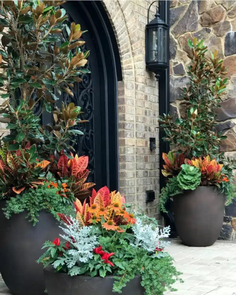Rustic stone farmhouse entrance with dark walls, tall planters, and colorful flowers arranged in layers