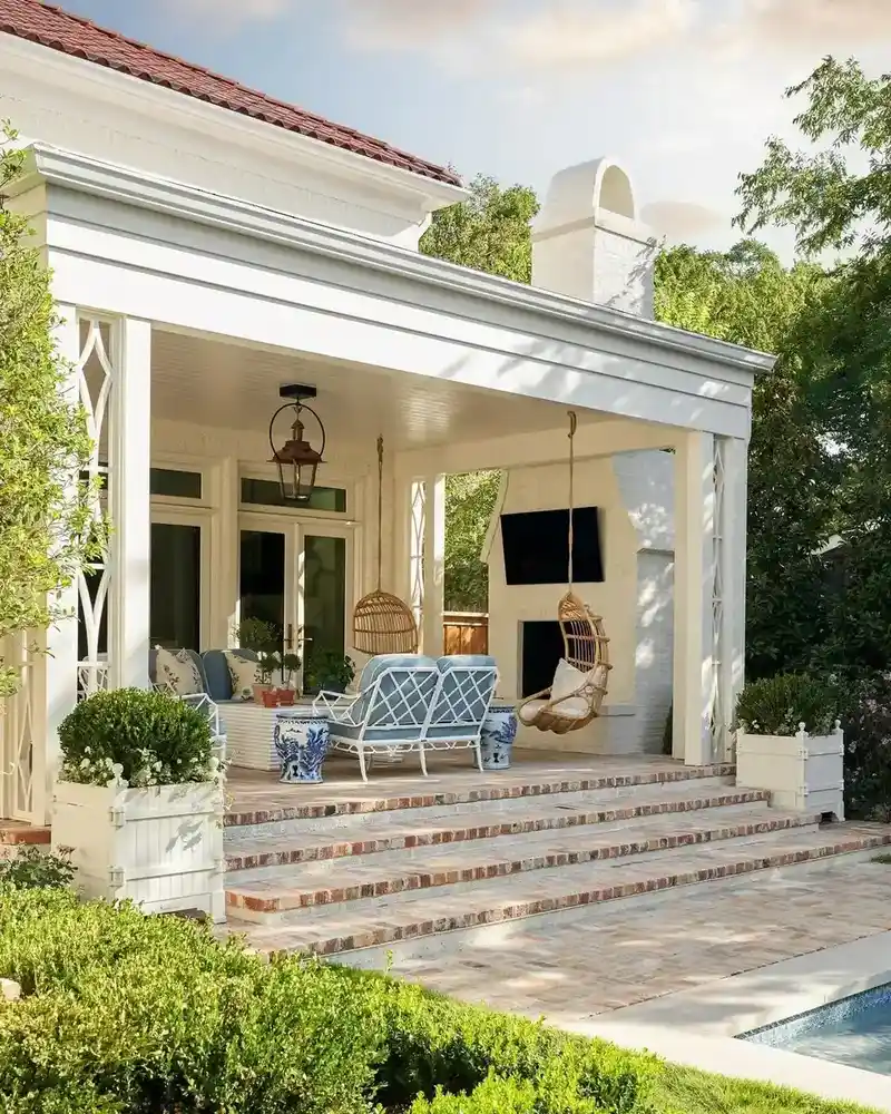 White architectural porch with columns, broad steps, simple seating, and white and green landscaping.