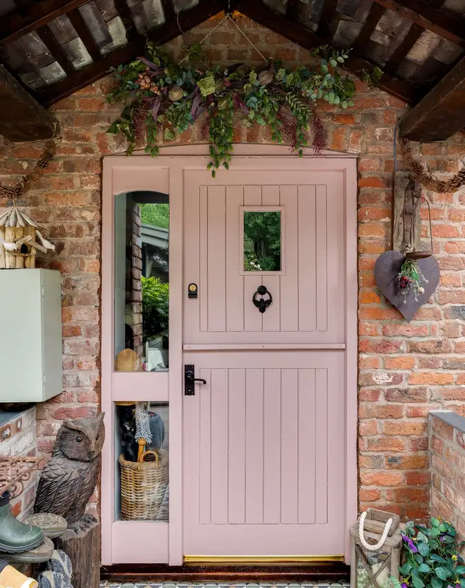 Pink front door framed by rustic brick walls and exposed wooden beams with a simple wreath