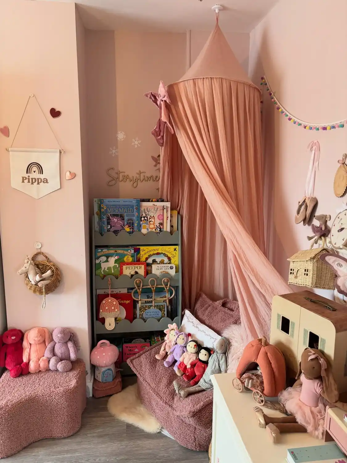 Kids bedroom reading corner with ceiling canopy, floor cushions, dolls, and front-facing book rack