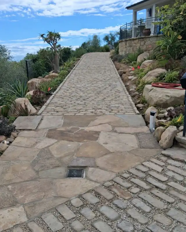 Irregular natural stone driveway with smaller stones and rustic landscaping on a sloped entrance