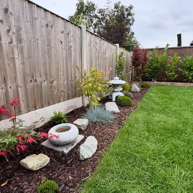 Japanese garden border beside a lawn with a stone lantern, pale gravel, rocks, and low plants