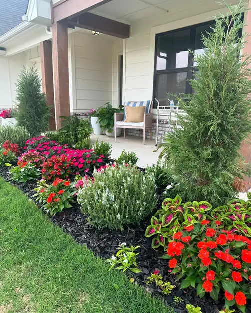 Front porch bordered by red flowers and taller green plants along the steps