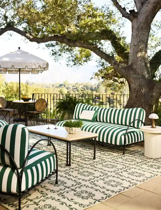 Green and white striped patio cushions paired with a pale patterned outdoor rug in a garden setting.