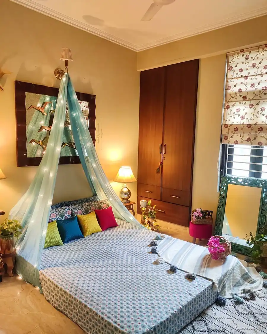Small bedroom with low bed, sheer canopy curtains, string lights and colorful cushions