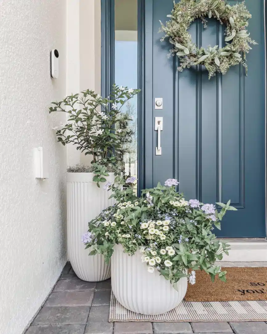 Small farmhouse entrance with a muted blue front door, leafy wreath, and large white planter