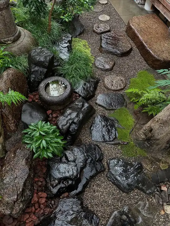Japanese garden stream with dark natural rocks, stone basins, and leafy plants