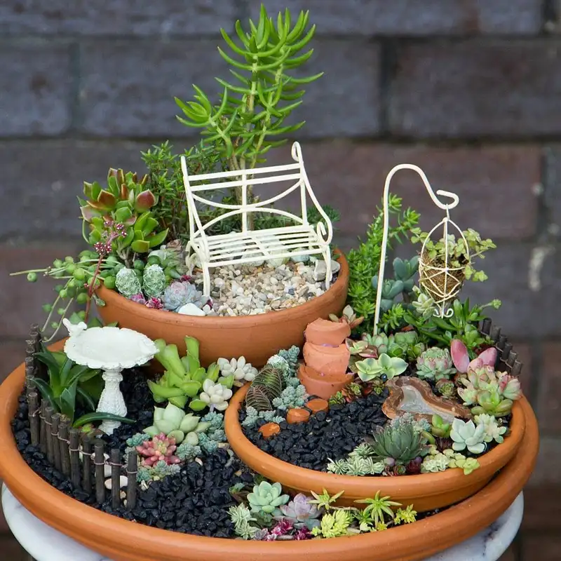 Miniature fairy garden with a tiny white chair, succulents, flowers, stones, and a watering can