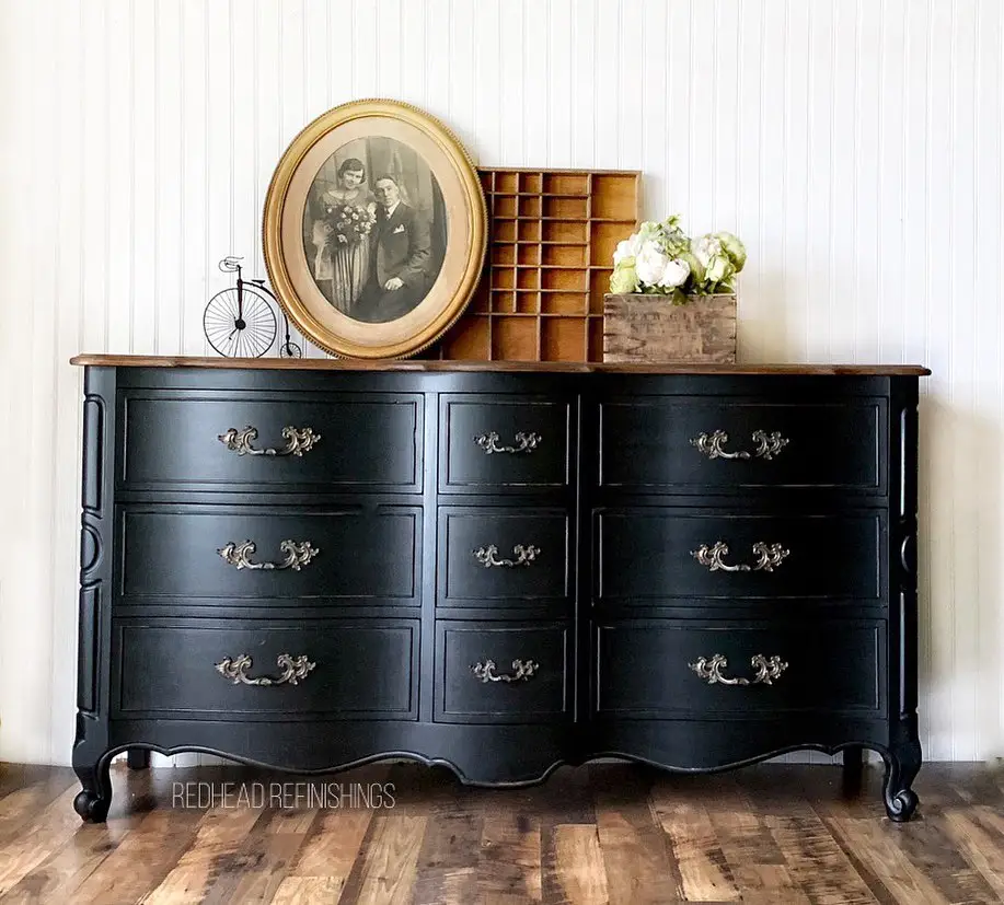 Vintage black dresser styled with oval portrait, wooden cubby, miniature bicycle, and white flowers