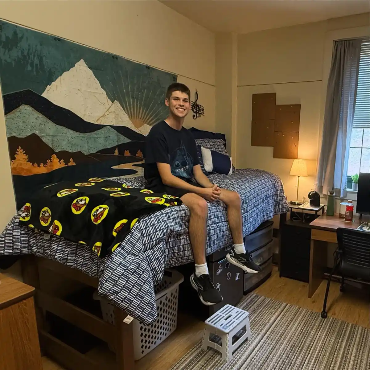 Dorm room with a large mountain mural, dark bedding, graphic blankets, and simple surrounding wall decor