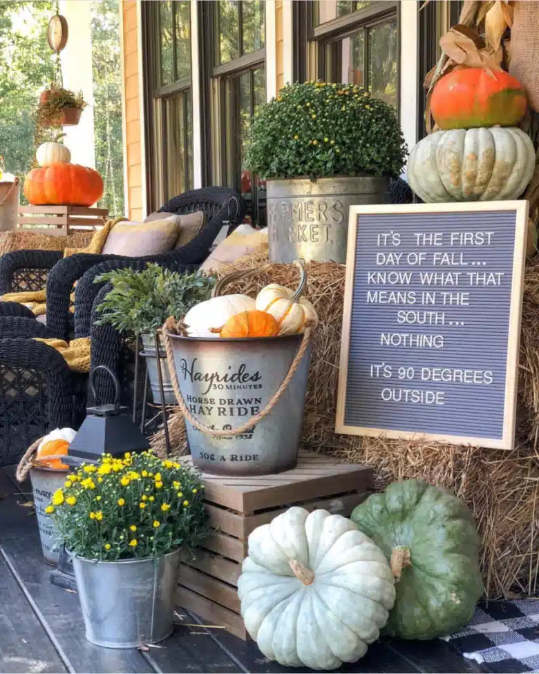 Fall farmhouse porch decorated with pumpkins, orange flowers, leafy plants, and a seasonal sign