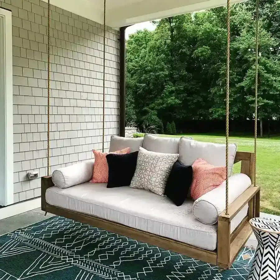 Small outdoor seating area with a pale sofa, colorful cushions, patterned rug, and lawn beyond.